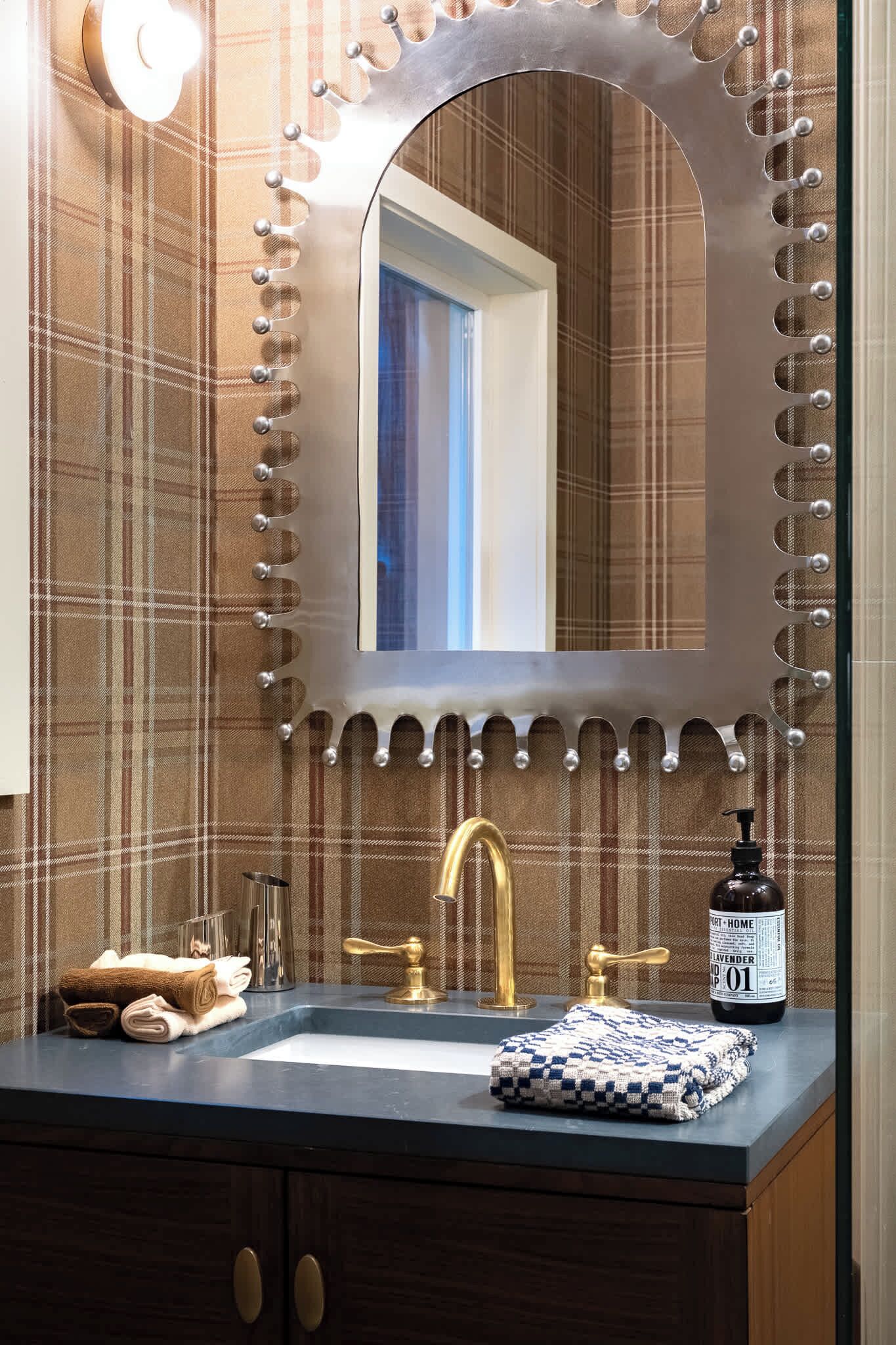 Un baño con tocador, espejo con luces decorativas, toallero y una botella de jabón de manos.