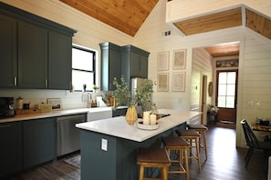 A kitchen with dark cabinets, a central island with stools, and framed pictures on the wall. - Summit Sky: Charming Luxury Cabin with Treetop Views in Hochatown, Broken Bow (Broken Bow)