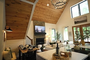 A cozy living room with a fireplace, wooden ceiling, and a television mounted on the wall. - Summit Sky: Charming Luxury Cabin with Treetop Views in Hochatown, Broken Bow (Broken Bow)