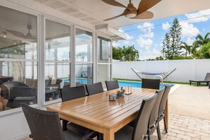 Eine überdachte Terrasse mit Pool, Esstisch, Stühlen und Deckenventilator.