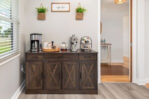 Eine Küchenzeile mit einem dunklen Holzschrank, einer Kaffeemaschine, einem Wasserkocher und einer Kaffeemühle auf der Arbeitsfläche.
