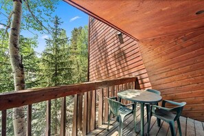 A wooden deck with a table and chairs, overlooking a forest. - Cimarron 203: Downtown Peak 9 Condo, Fireplace, Pool, Sauna & Hot Tub! (Breckenridge)