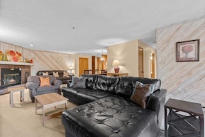 Ein Wohnzimmer mit Kamin, einer schwarzen Ledersofa, einem gemusterten Sessel und einem Holztisch.