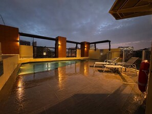 Ein Poolbereich auf dem Dach mit freiem Blick auf die Skyline der Stadt bei Einbruch der Dunkelheit.
