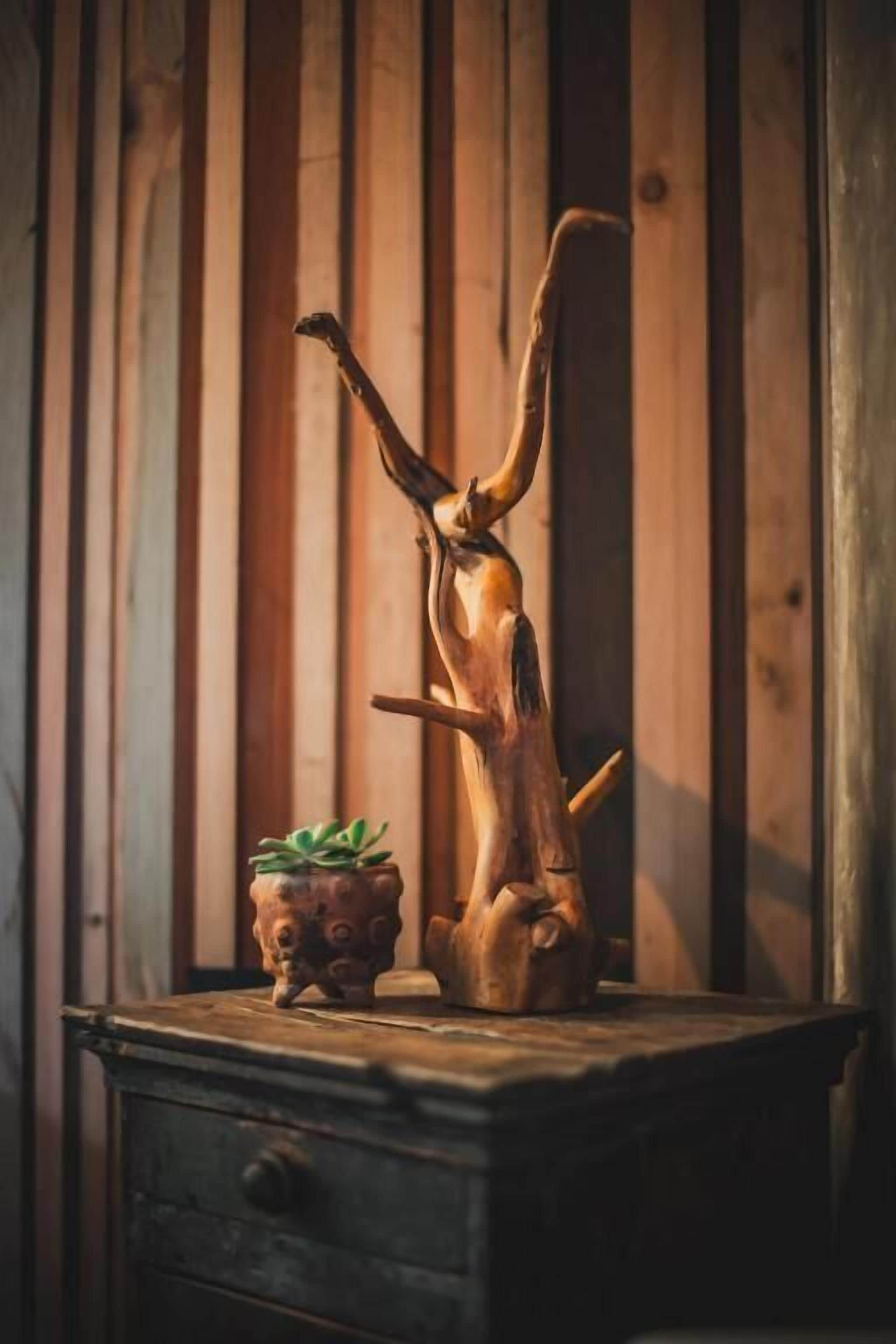 Una escultura de madera con una planta sobre un tocador frente a una pared de madera.