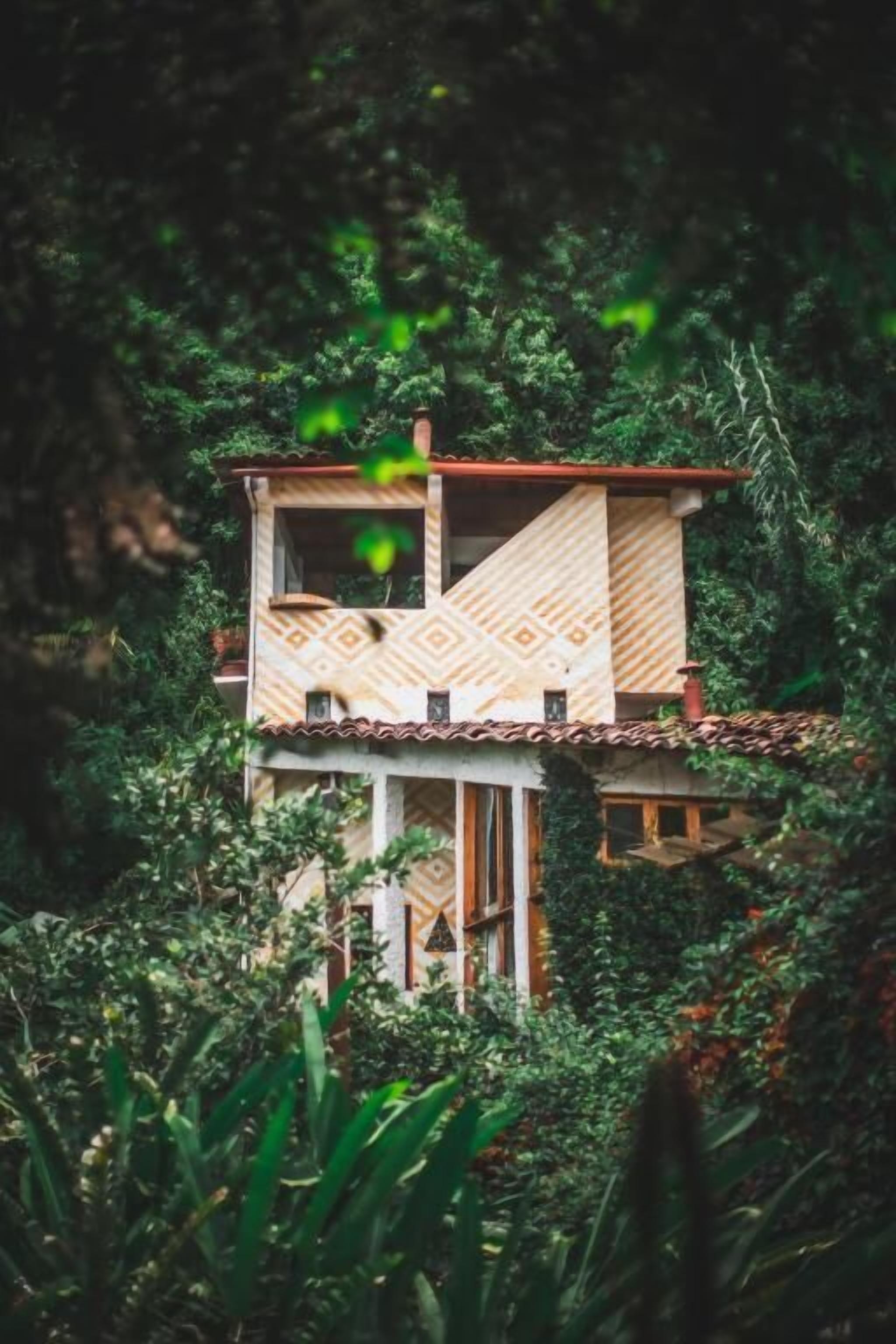 A model of a two-story building with a patterned facade, surrounded by dense foliage.