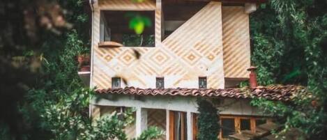 Modelo de un edificio de dos pisos con fachada decorativa, rodeado de follaje denso.