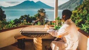 Eine Person sitzt an einem Tisch mit Blick auf einen Berg und ein Gewässer.