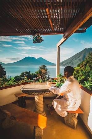 A person sitting at a table with a view of a mountain and a body of water.