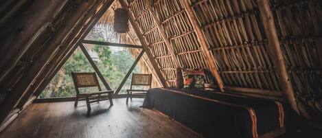 A triangular wooden room with a thatched roof, wooden floor, and a bench.