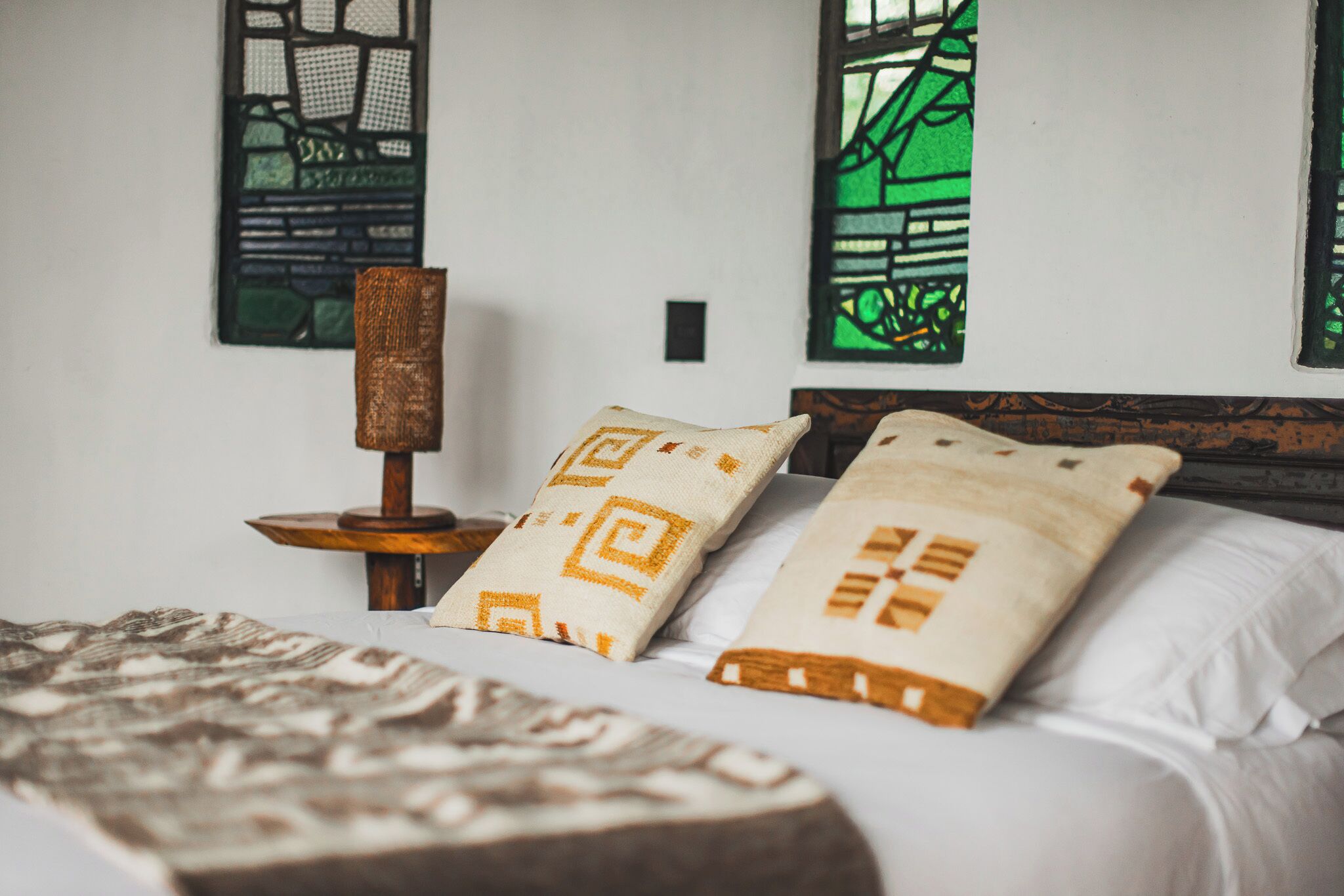 Un dormitorio con cama, almohadas, una mesita de noche y dos cuadros colgados en la pared.