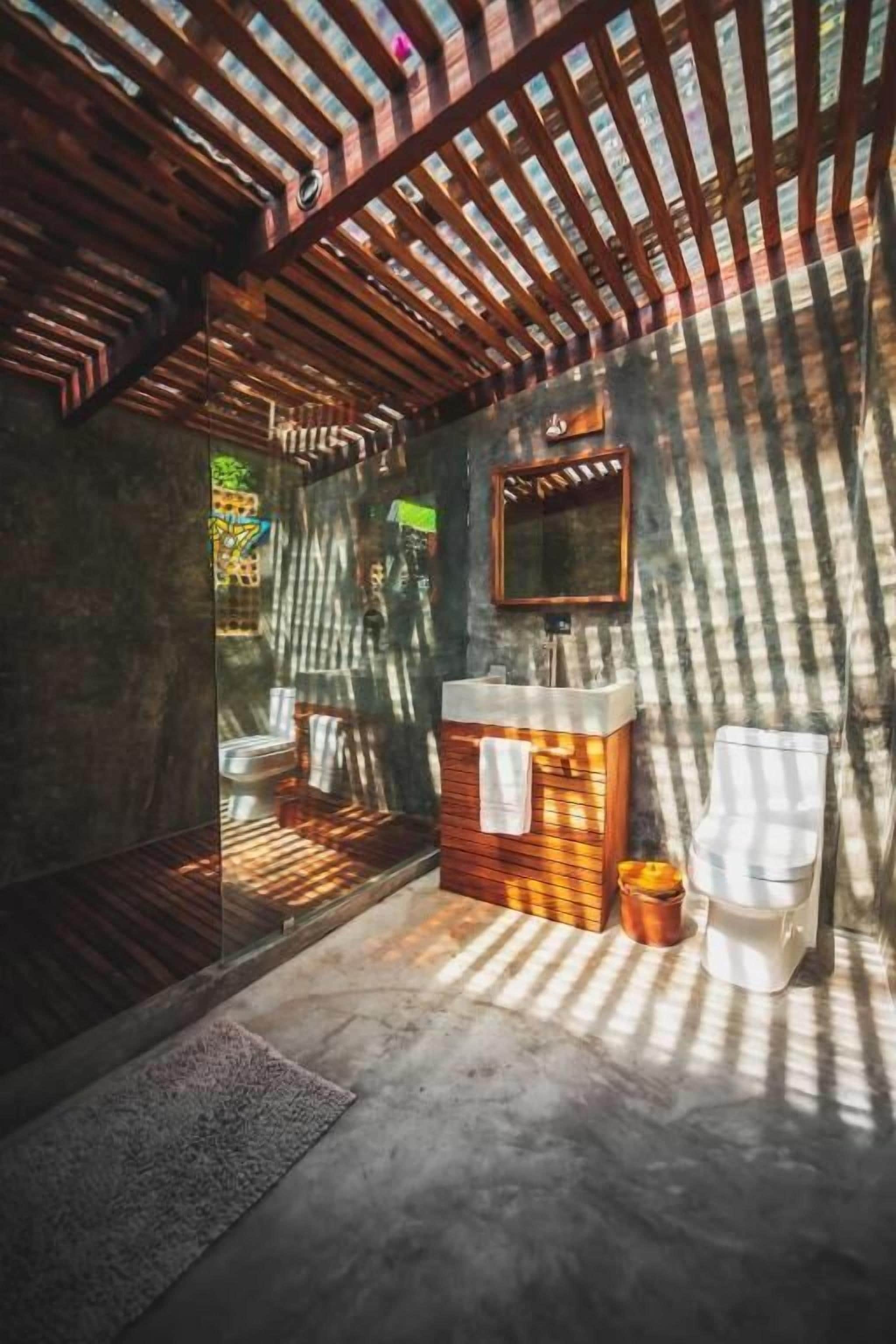A bathroom with a wooden vanity, a mirror, a toilet, and a glass shower enclosure.