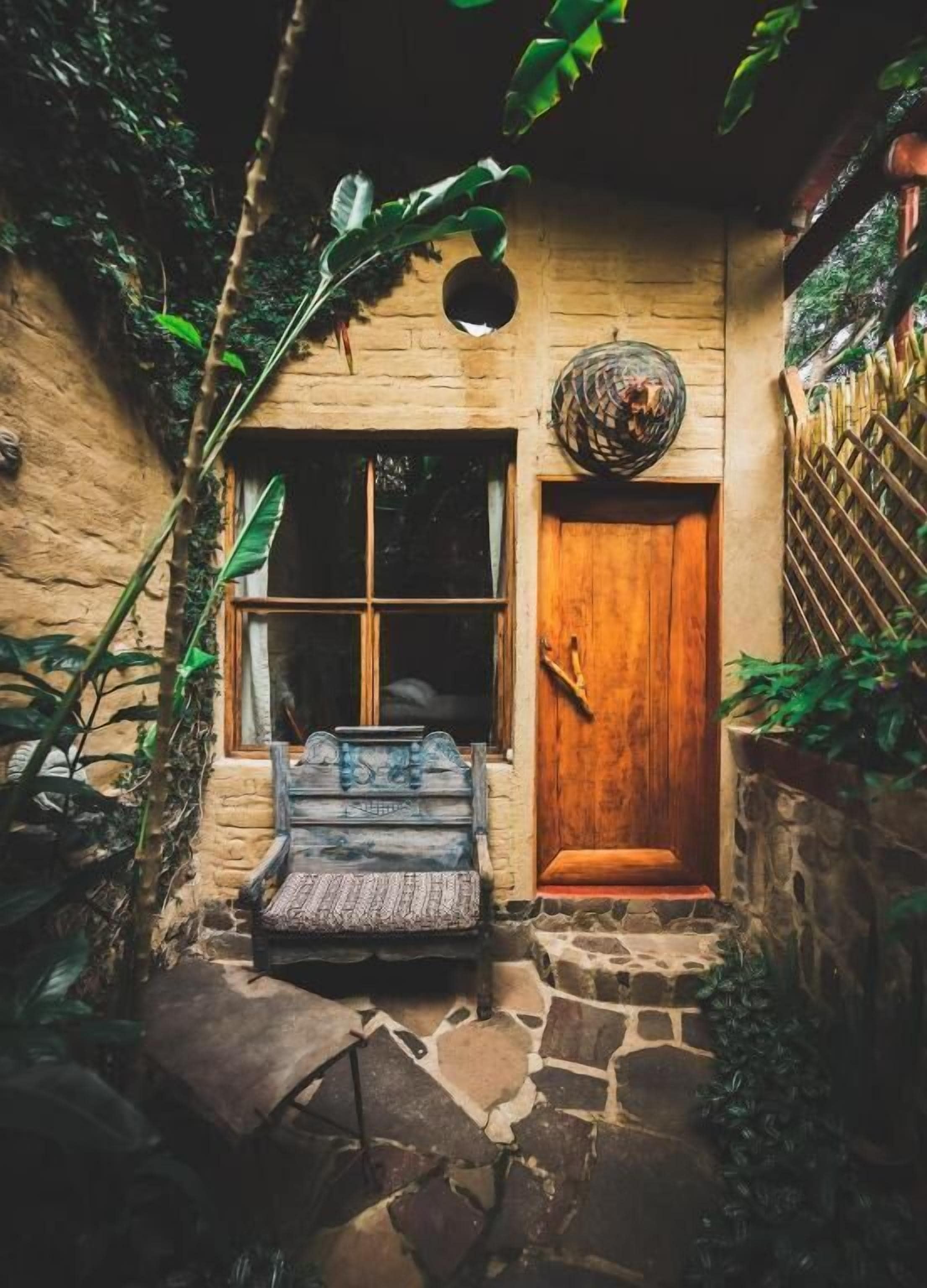Un edificio de paredes de piedra con una puerta y una ventana de madera, un banco afuera y una esfera decorativa sobre la puerta.