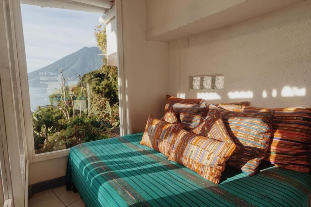 A bedroom with a bed, pillows, and a window with a view of a mountain and greenery.