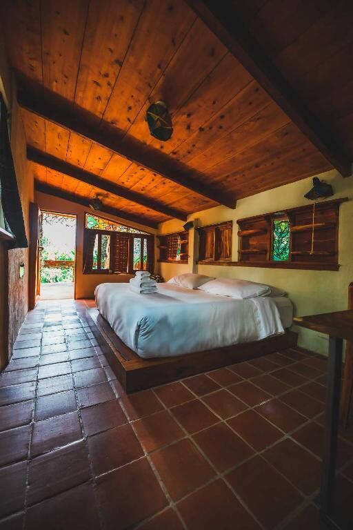 A wooden ceiling, a bed with pillows, a nightstand, and a window with a view.