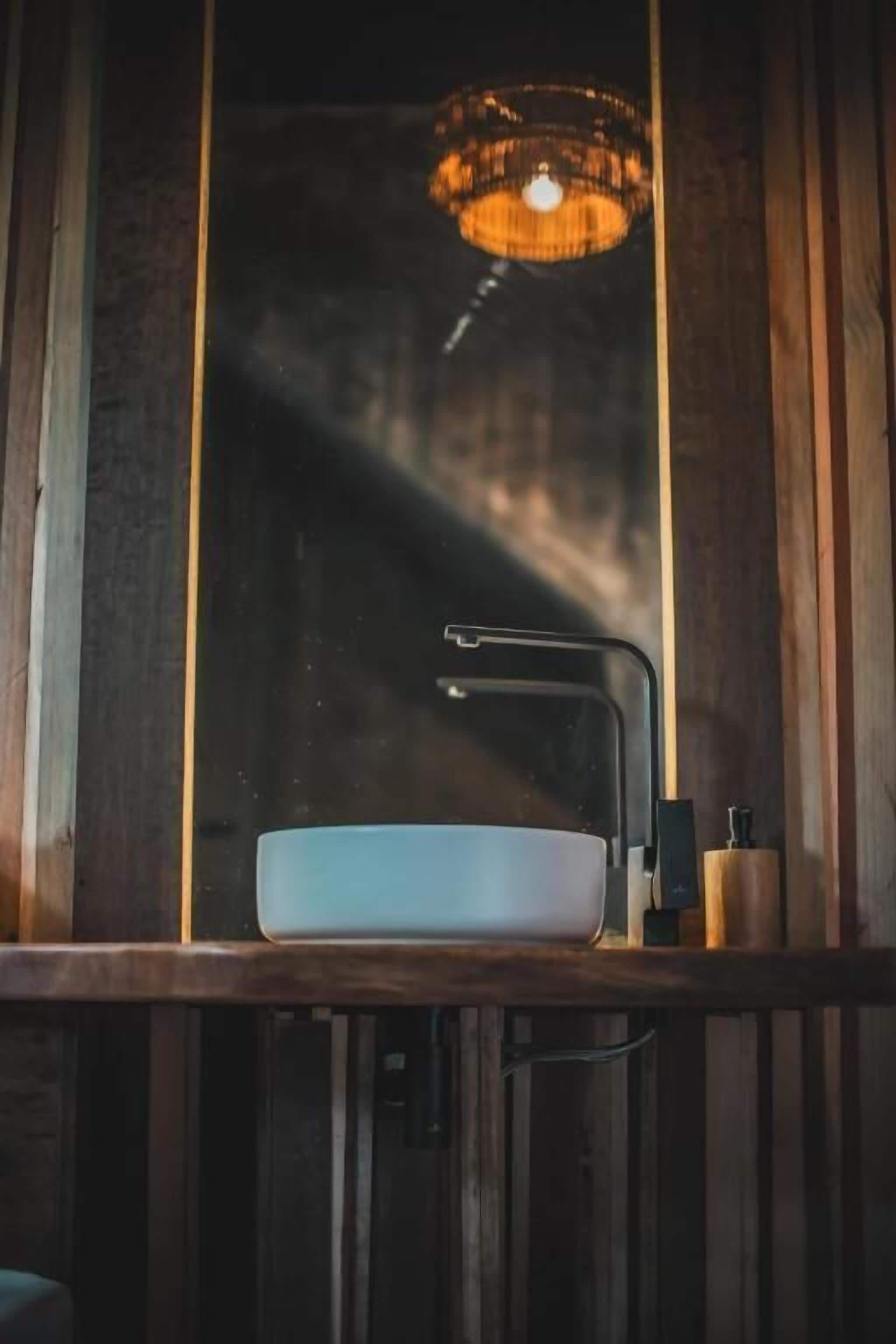 Une salle de bain avec un meuble-lavabo en bois, un lavabo blanc et un luminaire suspendu.