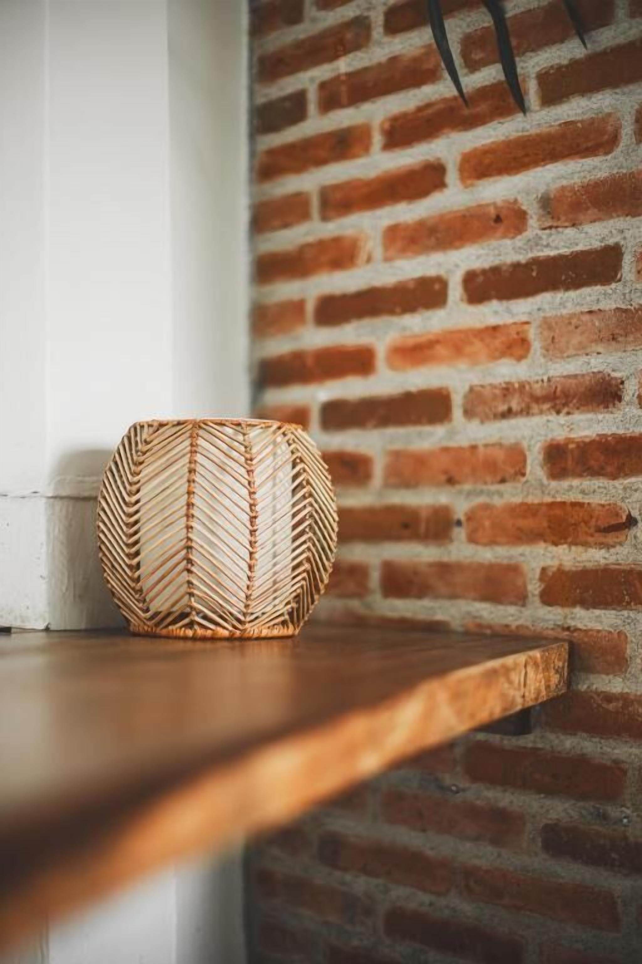 Una cesta tejida sobre un repisa de madera frente a un muro de ladrillo.
