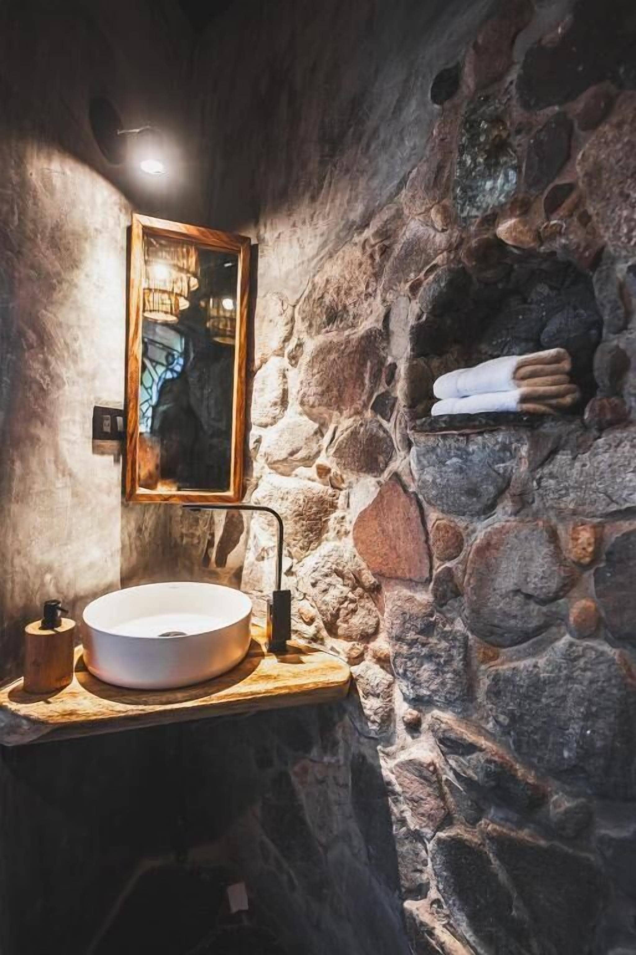 Un baño con paredes de piedra, un lavabo redondo, un espejo y un perchero para toallas.