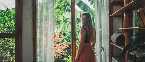 Una habitación con un ventanal grande, una cama y una estantería con plantas.