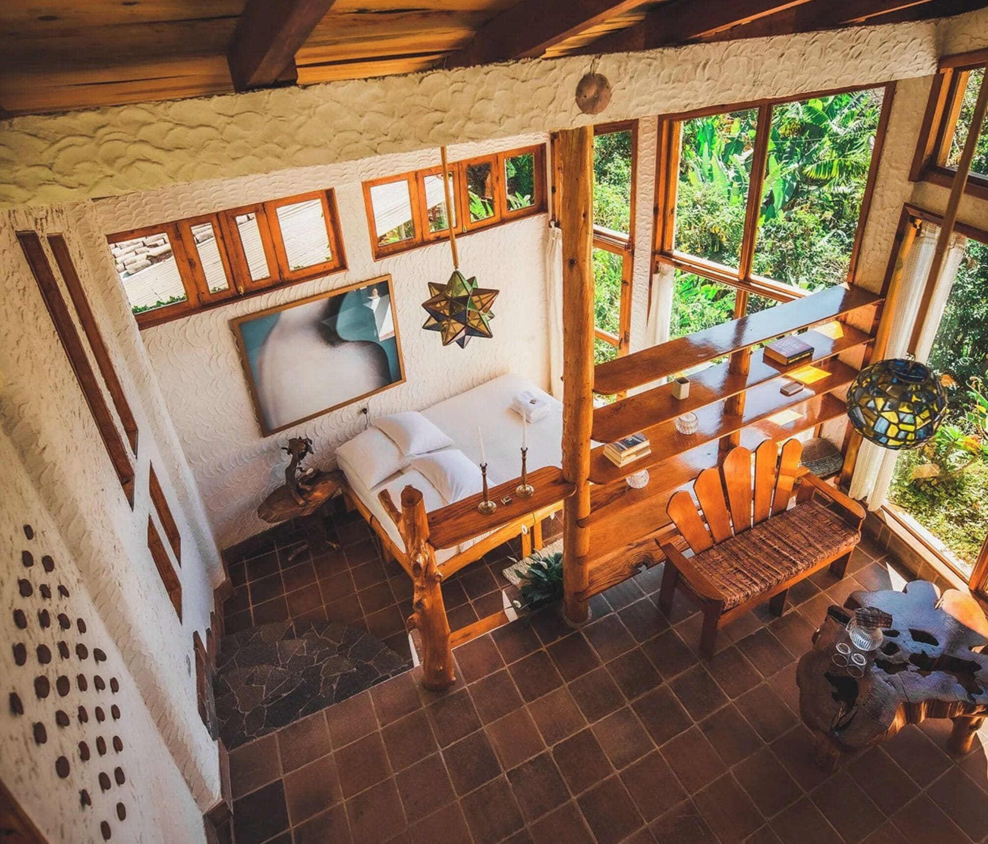 Habitación rústica con cama de madera, una mesita, una silla y un amplio ventanal con vistas a zonas verdes.