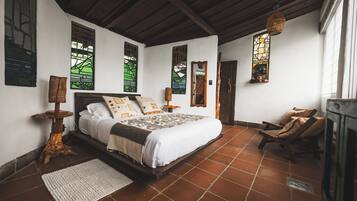 Quarto com cama, cadeira, mesa de cabeceira, abajur e janela.