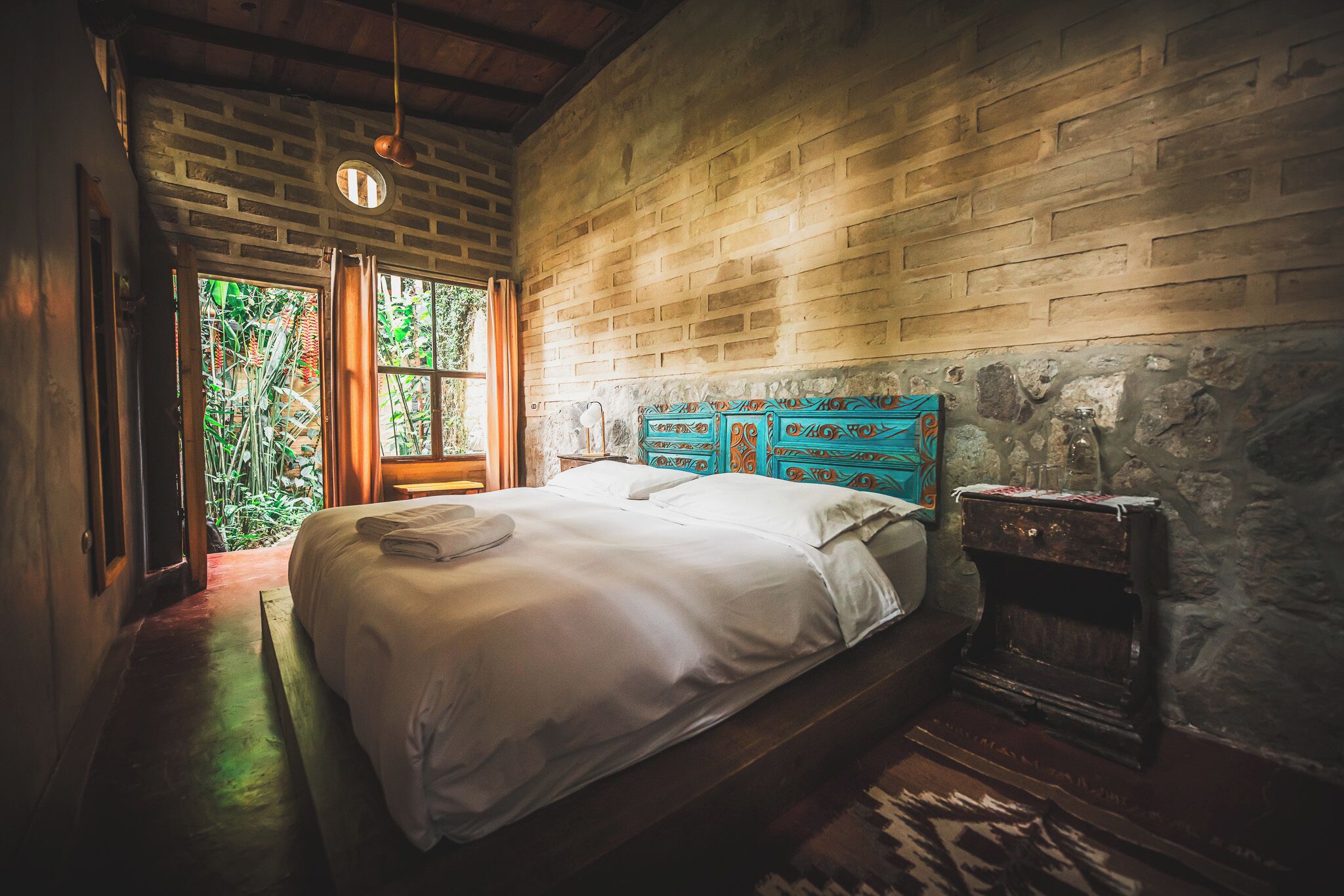 A room with a bed, a stone wall, and a window with curtains.