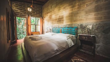 A room with a bed, a stone wall, and a window with curtains.