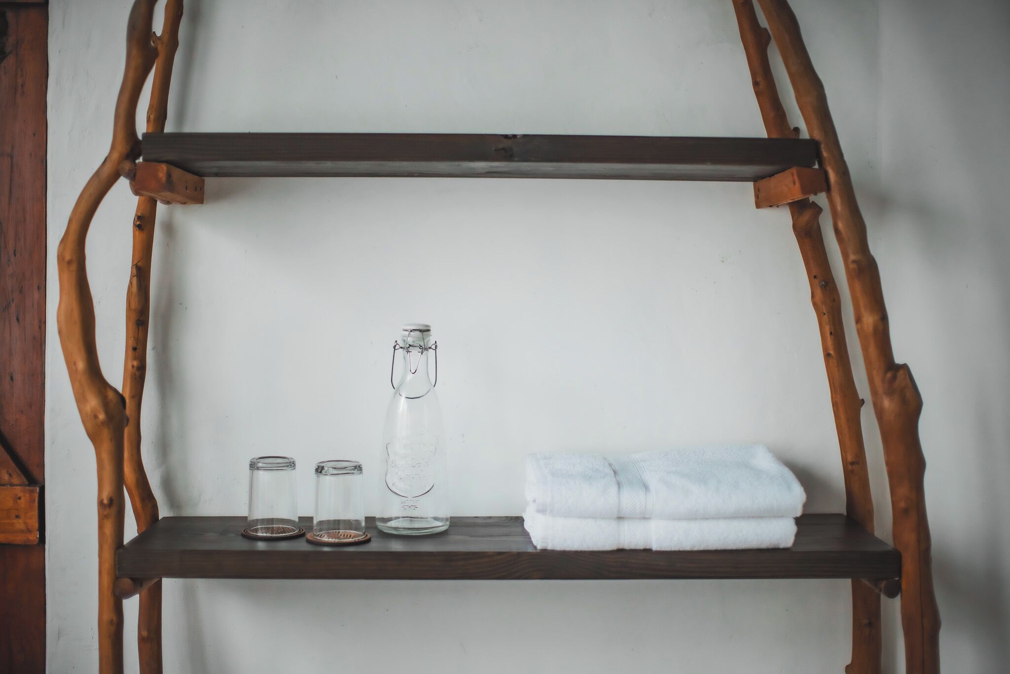A wooden shelf with glass containers and a towel against a plain wall.