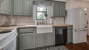 Une cuisine avec des meubles de couleur vert clair, un évier blanc, un réfrigérateur en acier inoxydable et un lave-vaisselle.