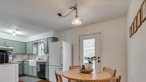 Une cuisine de taille réduite avec des meubles de couleur verte, un réfrigérateur blanc, une table à manger avec quatre chaises et un luminaire suspendu.