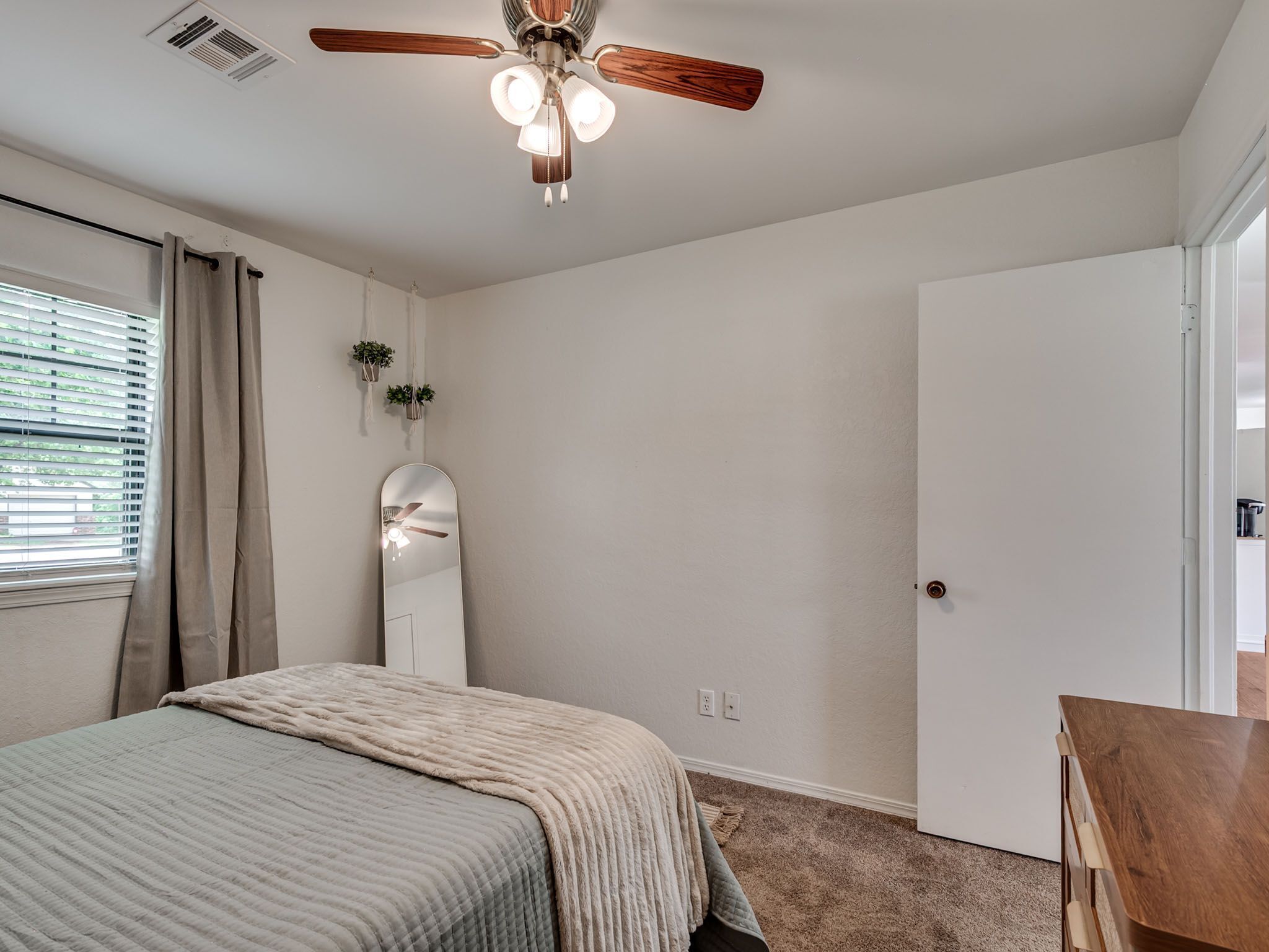 A bedroom with a bed, a ceiling fan, a door, and a window with curtains.