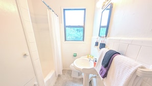 A bathroom with a bathtub, sink, and window. - The Flagler Flat | San Marco Gem (Jacksonville)