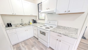 A modern kitchen with white cabinets, a granite countertop, a built-in oven, and a stainless steel sink. - The Flagler Flat | San Marco Gem (Jacksonville)