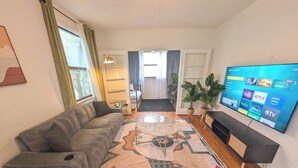 A living room with a sofa, a TV, a patterned rug, and a plant. - The Flagler Flat | San Marco Gem (Jacksonville)