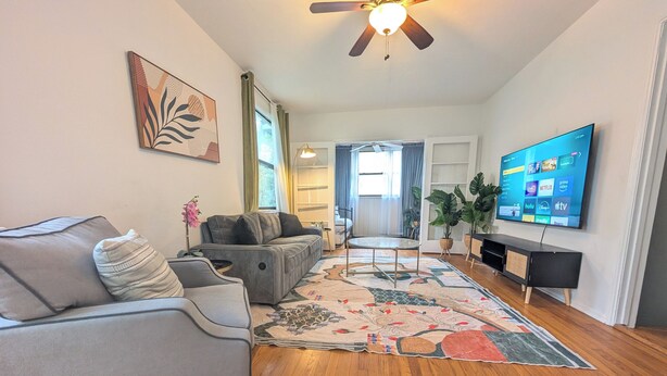 A living room with a sofa, a coffee table, a TV, and a ceiling fan. - The Flagler Flat | San Marco Gem (Jacksonville)