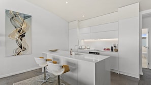 A modern kitchen with a central island, bar stools, and a contemporary art piece on the wall. - Skyline Serenity Two-Bedroom Waterfront (Auckland City)