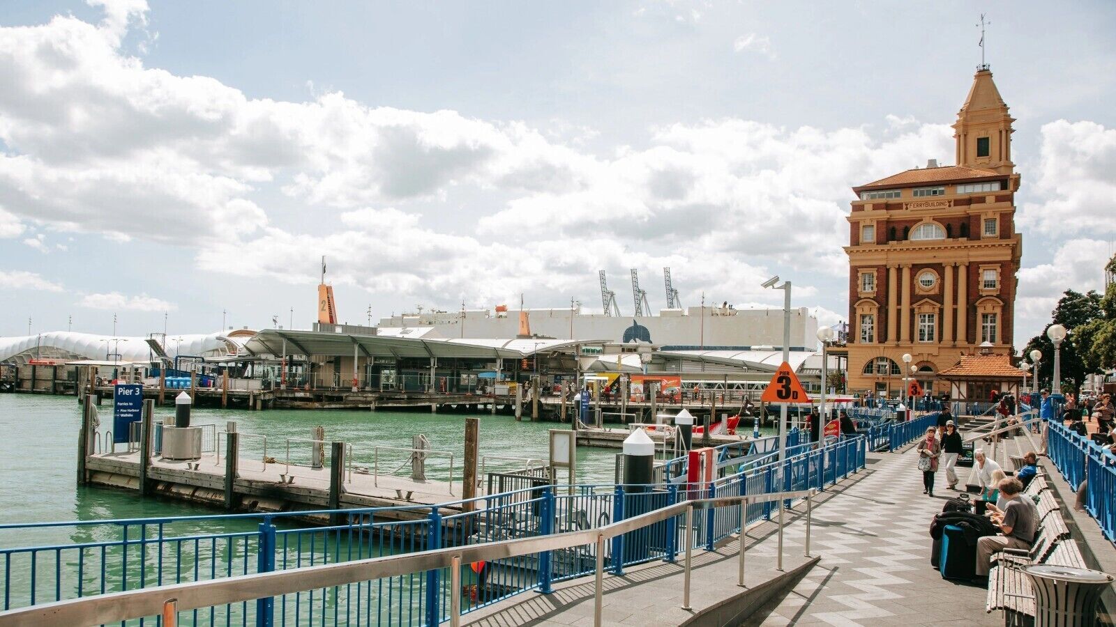 A waterfront pier with a historic building, a covered area, and a blue railing.