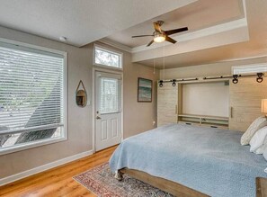 Ein Schlafzimmer mit Bett, Deckenventilator, Fenster mit Jalousien, einer Tür und einem kleinen Teppich.