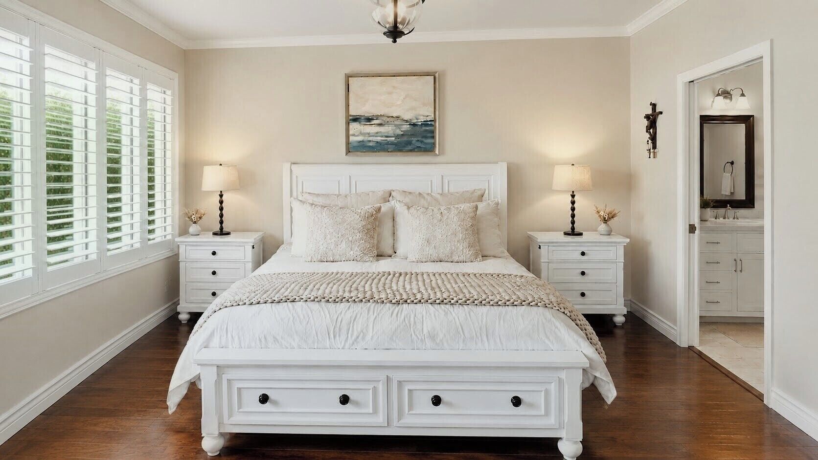 Une chambre à coucher avec un lit, deux tables de chevet, un tableau, et une salle de bain visible à travers une porte ouverte.