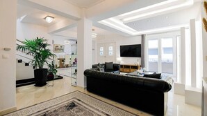 A modern living room with a black leather sofa, a flat-screen TV, and a large window. - Beach Blue Villa , Luxury 3-Bedroom Villa with Sea View (Korinthos)
