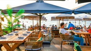 A beachside restaurant with wooden tables and chairs, umbrellas, and a view of the sea. - Beach Blue Villa , Luxury 3-Bedroom Villa with Sea View (Korinthos)