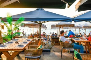 A beachside restaurant with wooden tables and chairs, umbrellas, and a view of the sea. - Beach Blue Villa , Luxury 3-Bedroom Villa with Sea View (Korinthos)