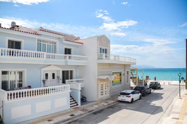 A two-story building with balconies, a beach view, and a parking area with cars.