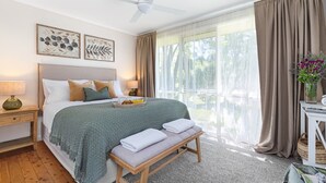 A bedroom with a bed, bedside tables, a bench, a window with curtains, and a view of the outdoors. - The Nook - central, cosy and well-equipped (Bowral)