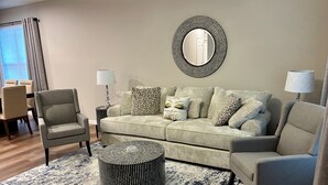 A living room with a sofa, armchairs, a coffee table, and a round mirror on the wall.
