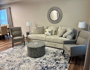 A living room with a sofa, armchairs, a coffee table, and a round mirror on the wall.