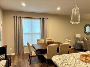 A dining area with a wooden table, beige chairs, a woven basket, and a hanging light fixture.