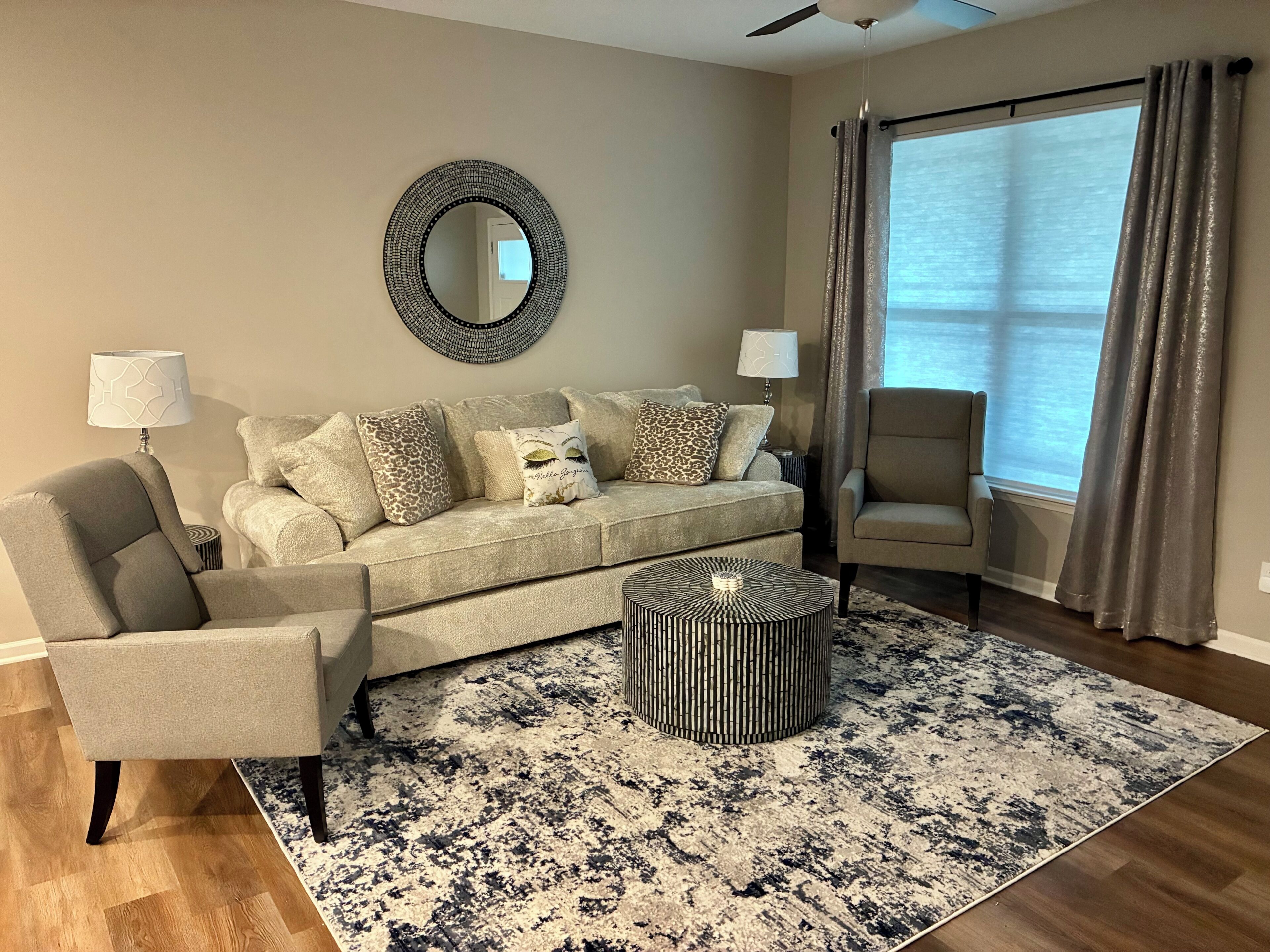 A living room with a sofa, armchair, round coffee table, and a large mirror on the wall.