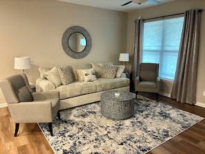 A living room with a sofa, armchair, round coffee table, and a large mirror on the wall.