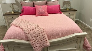 A bed with a pink quilt, a crocheted throw, and multiple pillows.